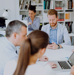 Group of professionals working together in an office setting, collaborating and using laptops and smartphones.