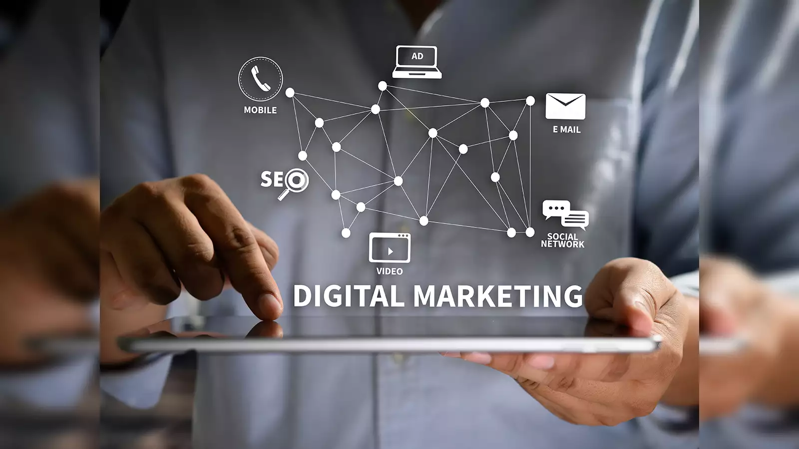 A close-up of a person using a tablet, with digital marketing-related icons and terms superimposed over the image. The icons represent various elements of digital marketing, including SEO, social networks, email, mobile, video, and advertising. These icons are connected in a web-like structure, symbolizing the interconnected nature of different digital marketing channels. The term "Digital Marketing" is prominently displayed below, highlighting the focus on strategies and tools for online promotion and engagement.
